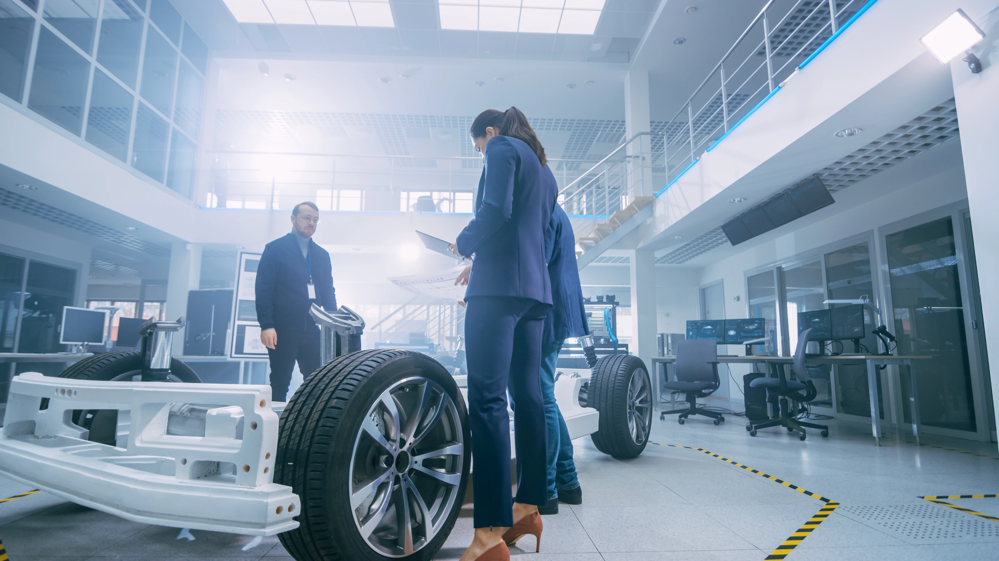 Drei Fachkräfte prüfen ein Fahrzeugchassis in einem modernen Labor.
