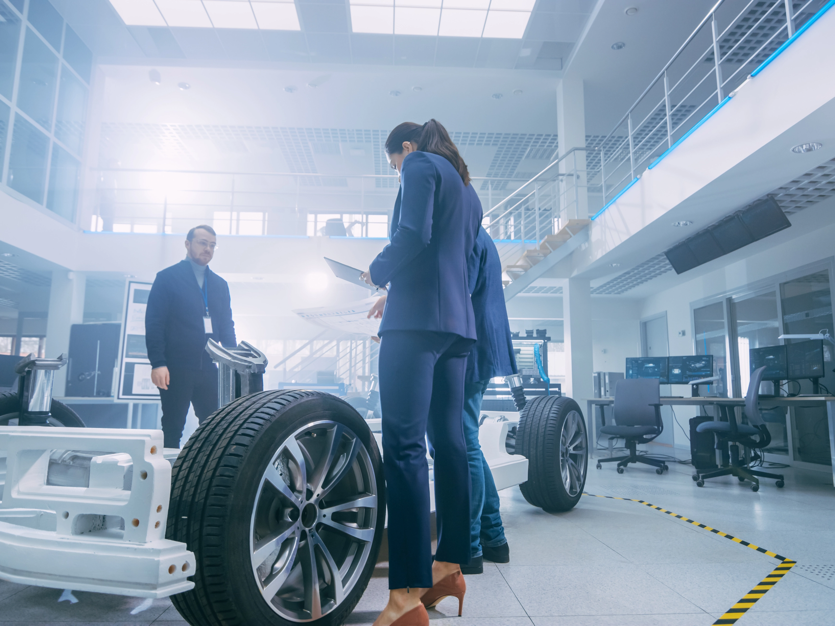 Drei Fachkräfte prüfen ein Fahrzeugchassis in einem modernen Labor.